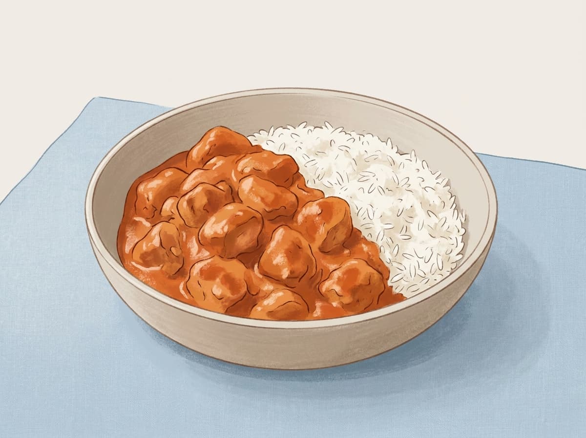 A bowl of butter chicken in a creamy orange sauce with rice